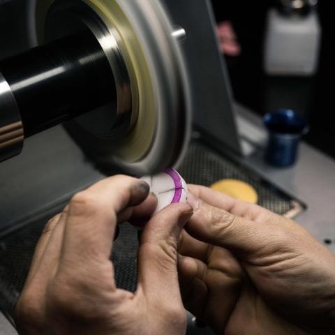 Photographie montrant les mains d'un ouvrier au travail de polissage d'une lunette de montre.